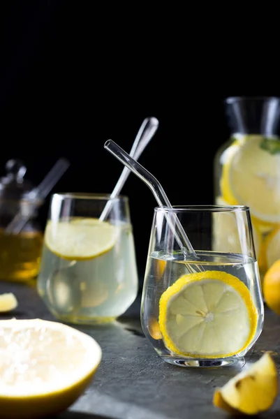 Two glasses of lemonade on a black background. Lemon slices and mint leaves float in the water and lie next to each other on the table