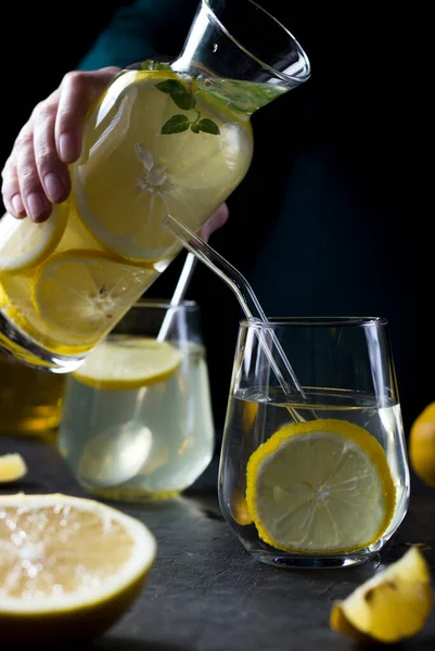 Two glasses of lemonade on a black background. Lemon slices and mint leaves float in the water and lie next to each other on the table