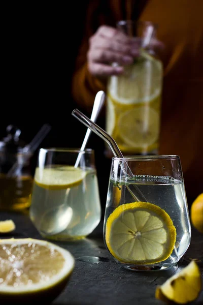 Two glasses of lemonade on a black background. Lemon slices and mint leaves float in the water and lie next to each other on the table