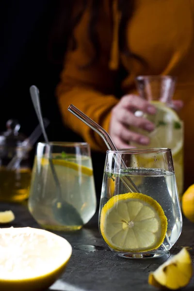 Two glasses of lemonade on a black background. Lemon slices and mint leaves float in the water and lie next to each other on the table