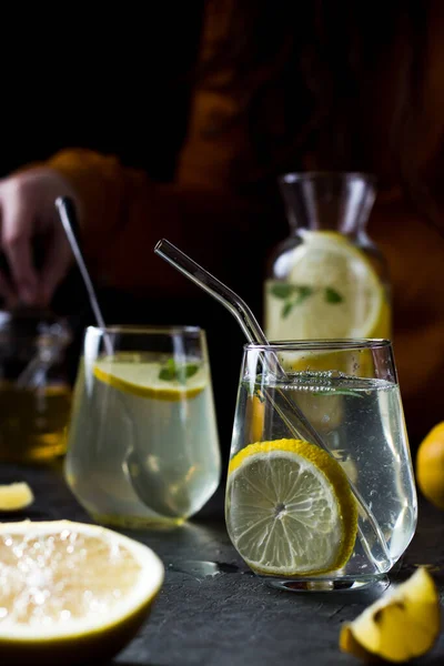 Two glasses of lemonade on a black background. Lemon slices and mint leaves float in the water and lie next to each other on the table