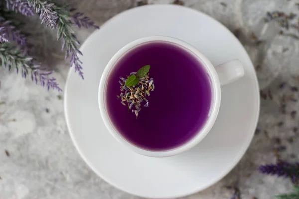 lavender tea in a white mug. Purple tea in a mug on a light background stands on the table next to lavender flowers. Dried lavender flowers are brewed in a Cup.