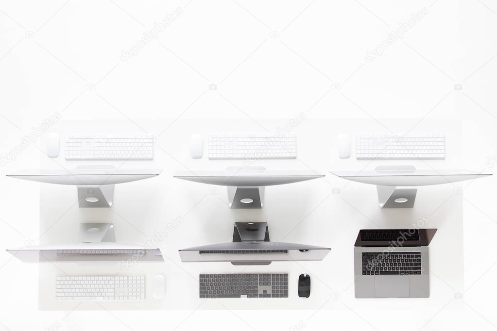 Group of new and modern computers put together on white desk, taken from high angle, top view.