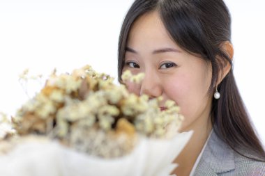 Genç Asyalı kız yüz mutlu bir şekilde beyaz bir arka plan üzerinde kahverengi bir çiçek tutan bir el gülümsüyor.