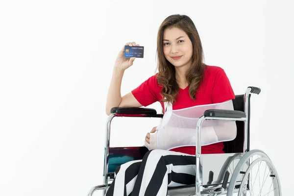 Broken Asian woman with arm sling sponsored in her hands sitting on a wheelchair Ideas for accident Injuries and health care studio photographed on a white background.