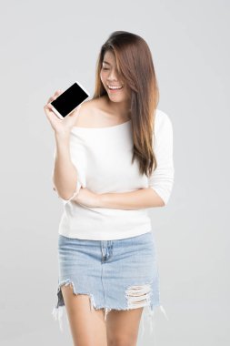 Genç güzel Asyalı kız stüdyo çekim gülümseme ve tutucu smartphone elinde duran beyaz arka plan üzerinde izole