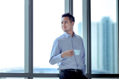 Karşı pencere elinde rahat duran Genç Asyalı bir fincan kahve göz önde işadamıdır.