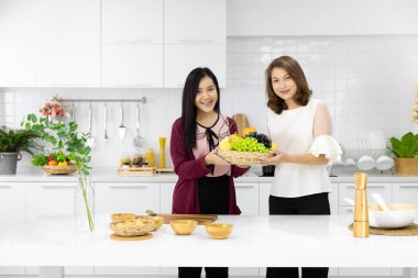 İki güzel genç ve dekorasyon için sahte sebze sepeti düzenlenmesi birlikte yeni modern mutfakta çalışan orta yaş Asyalı kadın. Aşk, Aile, anne ve kızı veya kardeşlik için kavramı.