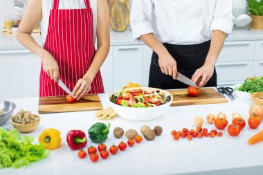 Beyaz modern mutfak Asya Şef tarafından öğretim güzel Asyalı kadın kırmızı önlük öğrenme nasıl yemek ve sebze salatası büyük kase içinde karıştırın.