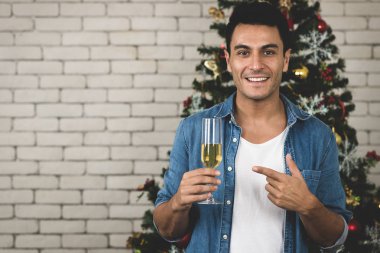 Mutlu beyaz adam Noel ile muhteşem gülümsemesi yüzünde, bardak beyaz şarap ile boşaltmak arkasında, glammorous Noel ağacı ile onun izlenim Noel'de gösterilen işaret eden keyif alıyor. Noel Tema.