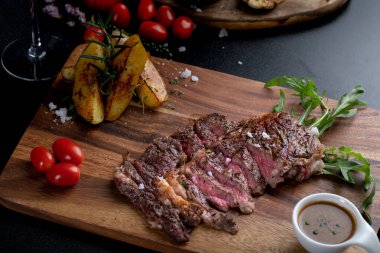 Medium rare meat rib eye steak slices in pan on chopping wooden board served with beef sauces look delicious. American style food. clipart