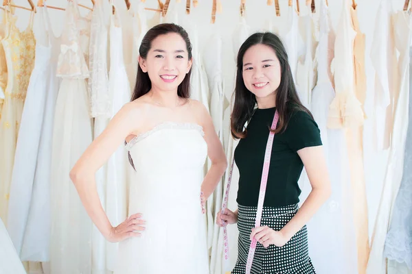 Portrait of bride customer and the wedding stylist are happy smiling at the camera, wedding dresses background.