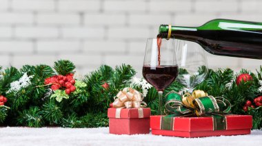 Kırmızı şarap, kırmızı hediye kutuları ve Christamas süsler ile dekorasyon cam şişe içinde yağıyor. Üst alan bulanık beyaz tuğla duvar ile de kopya alanı.
