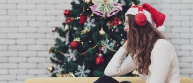 Genç beyaz Noel ağaçları arasında kanepede oturan ve hugh Noel ağacı önünde kulaklık ile müzik dinlemek kırmızı şapkalı. İyi zaman ve Noel günü mutluluk için kavram.