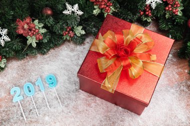 Bir çarpıcı kırmızı hediye kutusu altın şerit, Çamın dalları ve kırmızı holly Karpuzu sınır. Ahşap tahta ve bulanık mantık kar tanesi yıl 2019 mavi renk de dahil olmak üzere kopya alanı alt sol.