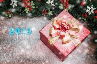 Bir çarpıcı kırmızı hediye kutusu altın şerit, Çamın dalları ve kırmızı holly Karpuzu sınır. Ahşap tahta ve bulanık mantık kar tanesi yıl 2019 mavi renk de dahil olmak üzere kopya alanı alt sol.