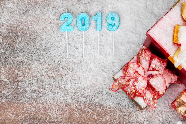 Year 2019 blue color overlay on wood board, red gift boxes at the side have snow all over, copy space bottom left.