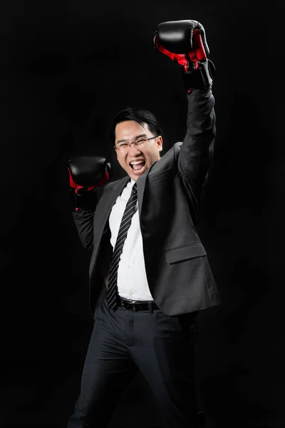 Asian man in formal suit and boxing gloves, exited smiling fight for achievement his target to be the winner and team successful. Champion of competition, the best of the year, challenge the business concept.