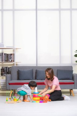 Mutlu Asya Aile, Genç, güzel annesi pembe bluz, yere, oturma içinde sarı ring, gri T-shirt, kısa, sevimli küçük yürümeye başlayan çocuk zevk topla oynamayı ve oyuncaklar oturma odası rahat tutun