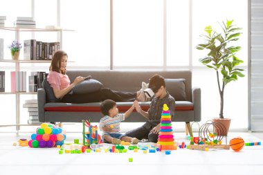 Asya Aile, tablet şakacı kanepeye, Genç çocuk giyim beyaz taklit Oyunlar gözlük kulaklık kullanma ev, genç güzel annem, rahatlatıcı, happy Time'da touch elleriyle küçük sevimli bebek