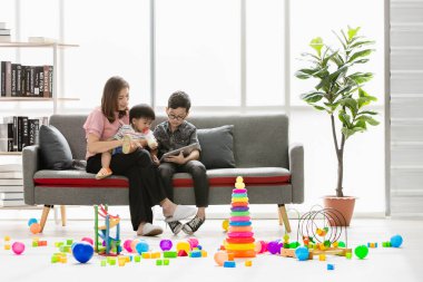 Asya Aile, mutlu, boş zaman evde, genç güzel annem gösteren kitap modern oturma odasında kollarında gözler gözlük takan genç oğlu süt şişeden içme sevimli, küçük yürümeye başlayan çocuk için