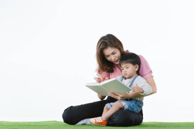 Asya Aile, mutlu zaman evde, onun tur üzerinde çok güzel toddler beyaz zemin üzerine yazmasını öğretim sevgiyle şirin, holding yapay yeşil çim üzerinde oturan genç güzel anne