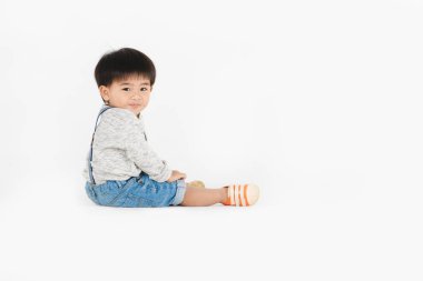 Stüdyonun sağ tarafında şirin, tapılası Asyalı bir çocuğun uzun kollu tişörtü, turuncu ayakkabısı ve izole edilmiş beyaz arka planda kameraya gülümseyen bir fotoğrafı var.