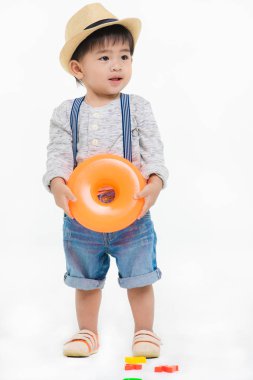 Stüdyo portresi. Saman şapkalı, kot tulumlu, parlak sarı şişirilebilir yüzük tutan, gülümseyen, izole beyaz bir arka planda yaşayan sevimli, tapılası bir çocuk.