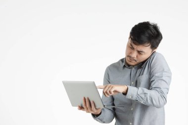 Varoluş stüdyo portre siyah saç, holding ve dijital tablet, üzgün, papatyanın yüz, smartphone, konuşurken işaret eden Genç Asyalı adam gri tişörtlü beyaz arka plan izole
