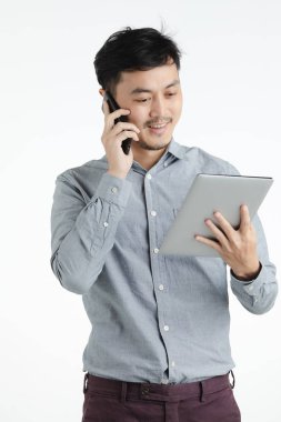 Varoluş stüdyo portre siyah saç, gülümseyerek ve seyir bir şey tablete, smartphone, konuşurken Genç Asyalı adam gri tişörtlü beyaz arka plan izole