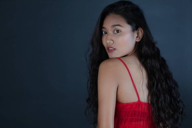 Varoluş stüdyo portre içinde kırmızı çıplak omuz, Asya genç güzel, uzun, kıvırcık siyah saçlı kadın, eğik kafa, kamera, koyu arka plan üzerinde uzak seyir dönüşü