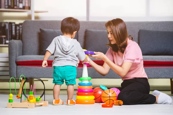 Mutlu Asya Aile, pembe bluz oturan kat, oğlu ile oynarken, gri T-shirt, kısa, sevimli küçük yürümeye başlayan çocuk, genç güzel anne topu ve rahat oturma odasında oyuncakları ile oynarken zevk