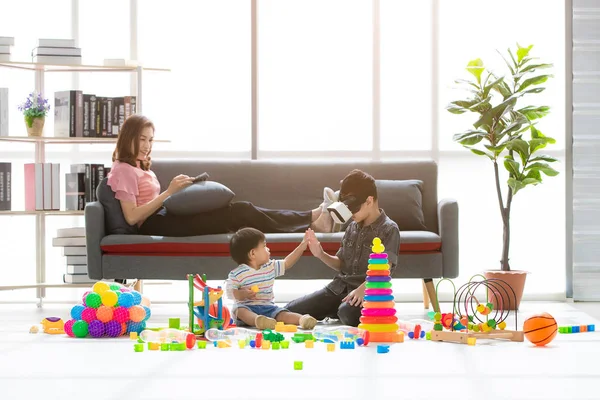 Asian family, happy time at home, young beautiful mother, relaxing, using tablet on couch, young boy wear white imitation games goggles headset playfully touch hands with little adorable toddler