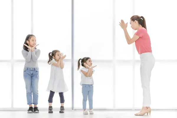 Asian woman in pink shirt teach children to playing something , they stand in front of big white window.