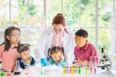 Fen bilgisi öğretmeni cam kase, renkli tüp ve laboratuvar Oda tabloda, kavram mikroskobunun çalışma laboratuvar odasında için Asya öğrenciler kimyasallar, öğretmen pour kimyasallar hakkında öğretmek.