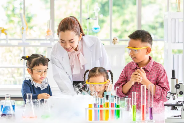 Science teacher teach Asian students about chemicals, smoke float out from blow, colorful test tube and microscope on table in laboratory room, concept for study in laboratory room.