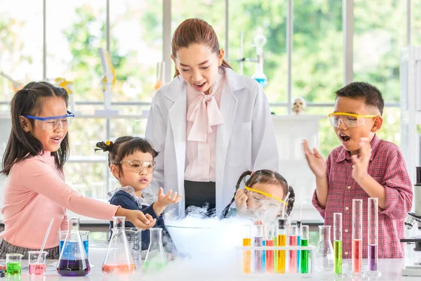 Science teacher teach Asian students about chemicals, smoke float out from blow, colorful test tube and microscope on table in laboratory room, concept for study in laboratory room.