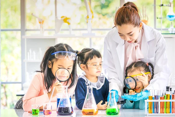科学老师在实验室教亚洲学生 老师用放大镜看东西 五颜六色的试管和桌子上的显微镜 在实验室学习的概念 — 图库照片