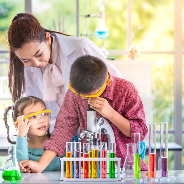 Science teacher teach Asian students in laboratory room, teacher look through microscope, colorful test tube and microscope on table , concept for study in laboratory room.