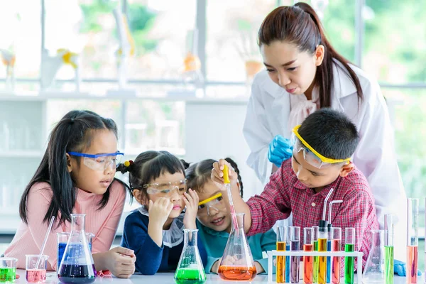 科学老师在实验室教亚洲学生 男孩把东西掉进橙色的管子里 五颜六色的试管和桌子上的显微镜 在实验室学习的概念 — 图库照片