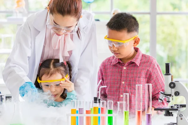 Science teacher teach Asian students in laboratory room, smoke float out of bowl, they excited, colorful test tube and microscope on table in laboratory room, concept for study in laboratory room.