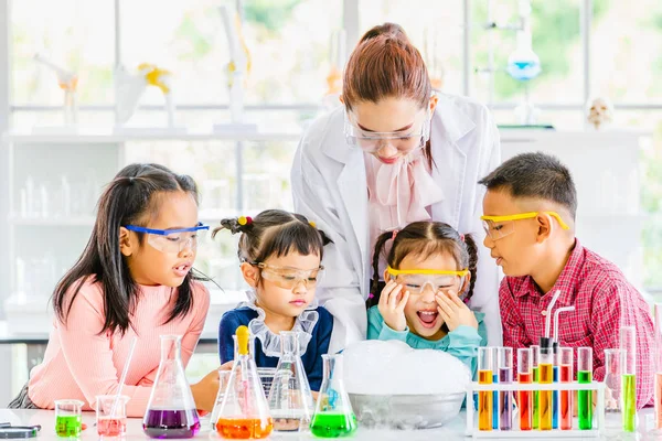 Science teacher teach Asian students in laboratory room, smoke float out of bowl, they excited, colorful test tube and microscope on table in laboratory room, concept for study in laboratory room.