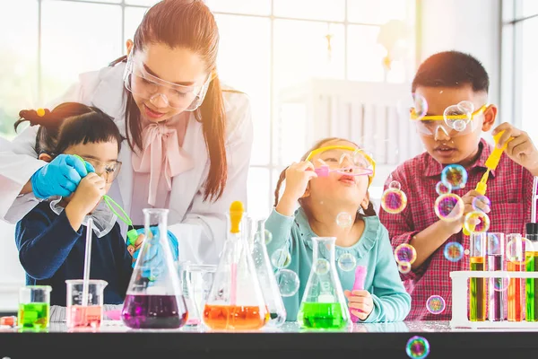Science teacher and Asian students in laboratory room, they blowing bubbles, colorful test tube and microscope on table in laboratory room, concept for study in laboratory room.