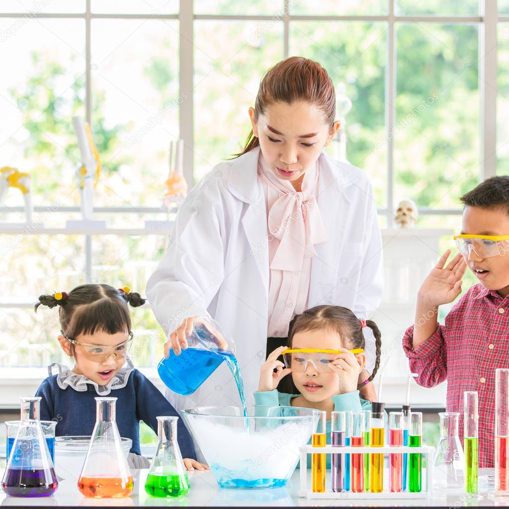 Science teacher teach Asian students about chemicals, teacher pour chemicals into glass bowl, colorful test tube and microscope on table in laboratory room, concept for study in laboratory room.