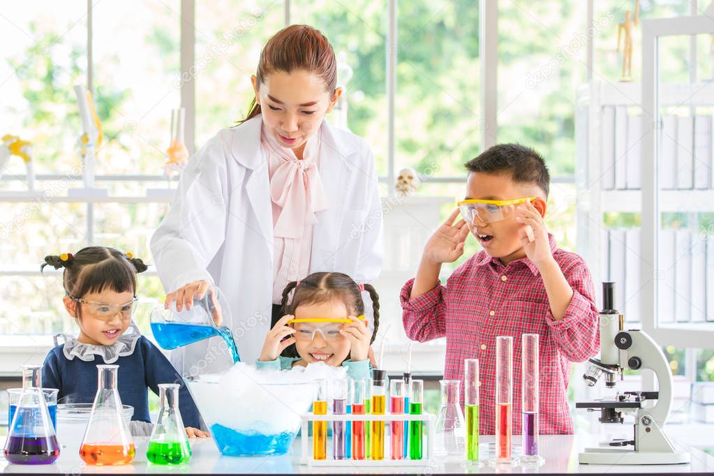 Science teacher teach Asian students about chemicals, teacher pour chemicals into glass bowl, colorful test tube and microscope on table in laboratory room, concept for study in laboratory room.