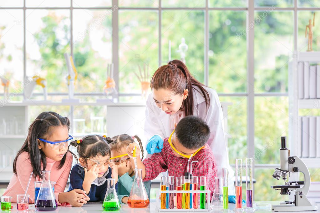 Science teacher teach Asian students in laboratory room, boy drop something into orange tube, colorful test tube and microscope on table , concept for study in laboratory room.