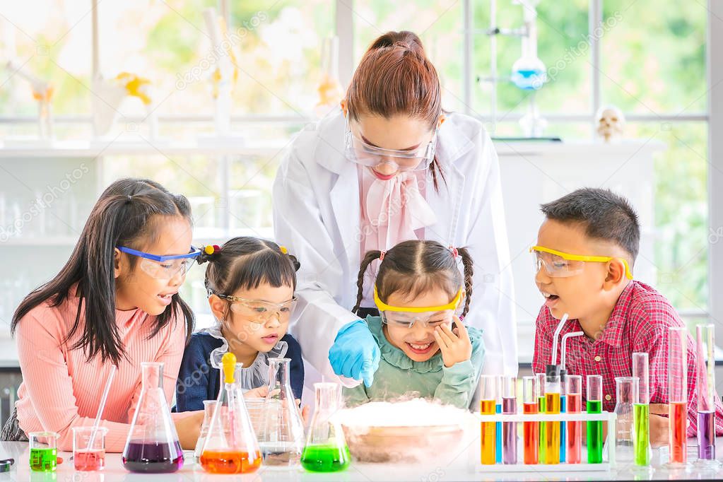 Science teacher teach Asian students in laboratory room, smoke float out of bowl, they excited, colorful test tube and microscope on table in laboratory room, concept for study in laboratory room.
