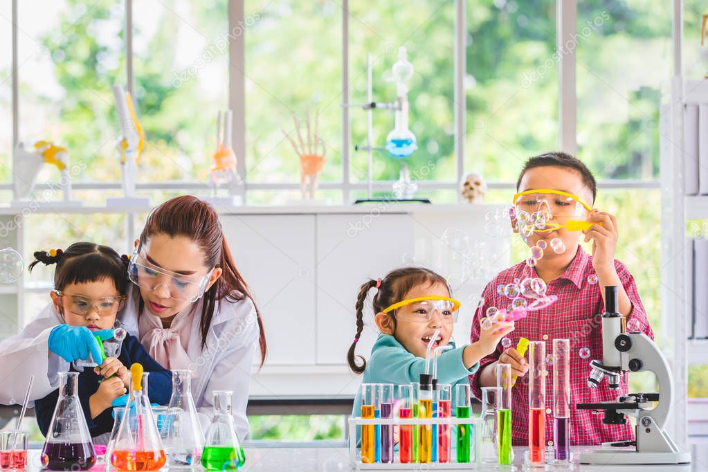 Science teacher and Asian students in laboratory room, they blowing bubbles, colorful test tube and microscope on table in laboratory room, concept for study in laboratory room.