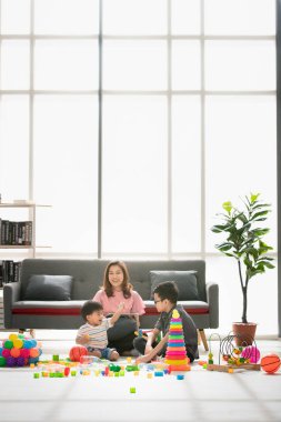 Asya Aile, boş zaman evde, genç güzel annem, rahatlatıcı, tablet kanepe, iki çocuk birlikte katta parlak ışık, rahat oturma odası çok renkli oyuncakları ile oynarken zevk kullanma.