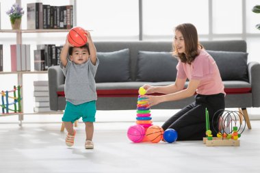 Mutlu Asya lı aile, pembe bluzlu genç güzel anne, yerde oturuyor, oğluyla oynuyor, gri tişörtlü sevimli küçük çocuk, kısa, rahat oturma odasında birlikte zaman geçirebilirler.